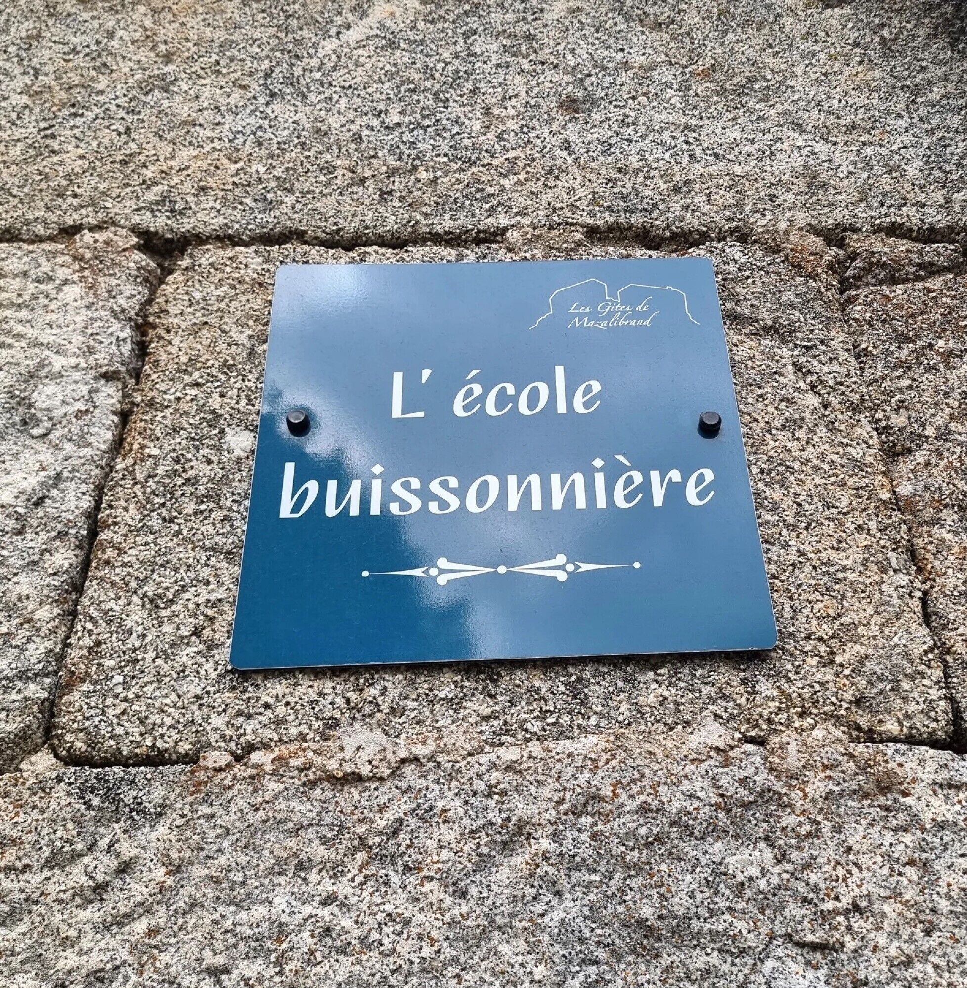 A sign on a stone surface with the text 'L'école buissonnière' and a logo.