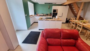 A modern kitchen with white cabinets, a black oven, and a dining area with wooden chairs and a table. - Cottage “L'École Buissonnière de Mazalibrand”: Mountain View, Private Terrace & Garden (Mazet-Saint-Voy)