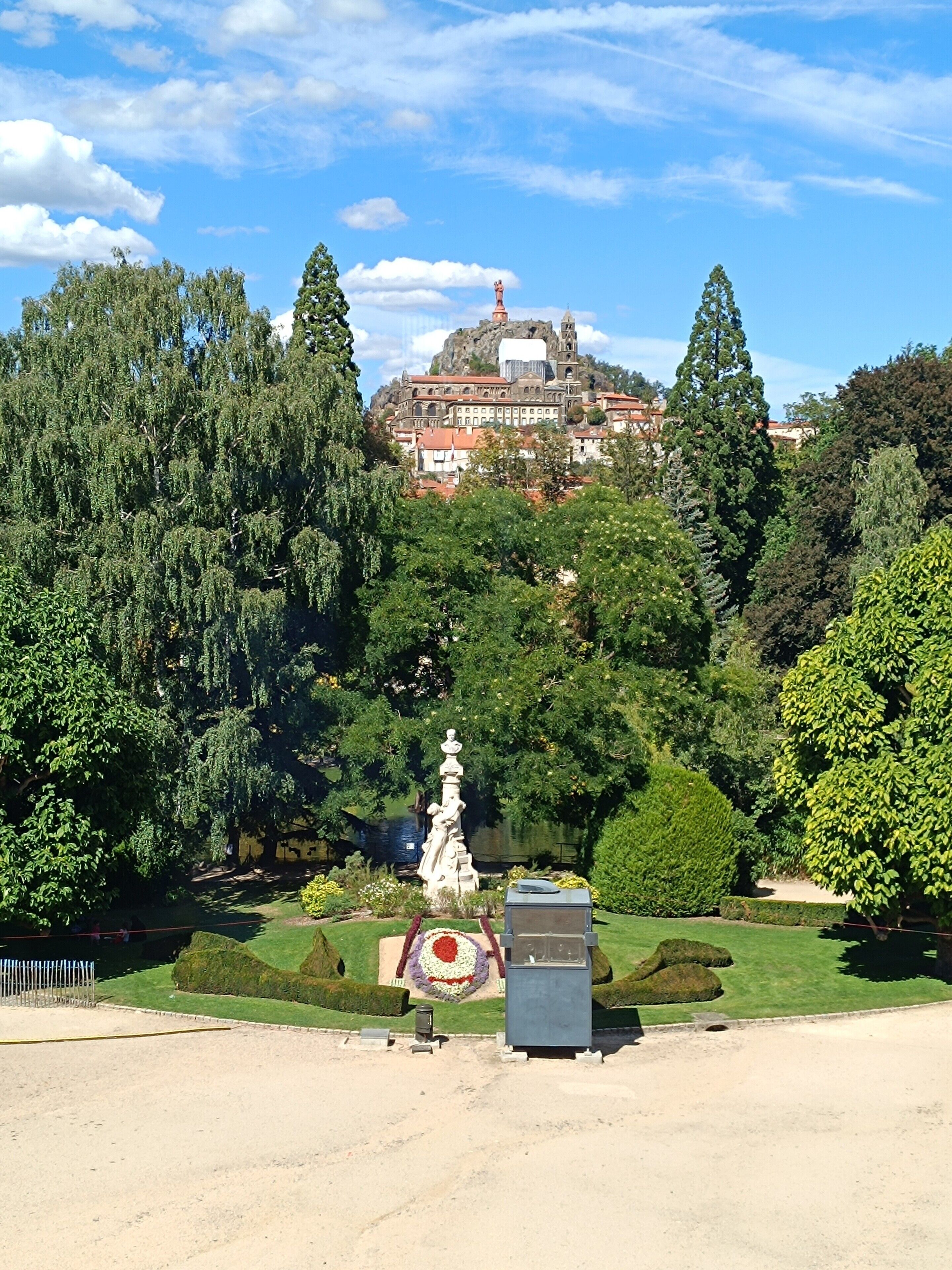 Un parque con una estatua, un edificio con un campanario y un estanque.