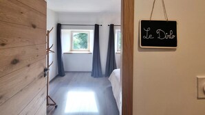 A room with a wooden wall, a window with curtains, a bed, and a sign on the wall. - Cottage “L'École Buissonnière de Mazalibrand”: Mountain View, Private Terrace & Garden (Mazet-Saint-Voy)