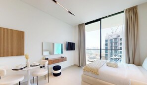 A modern hotel room with a bed, a desk, a chair, a small table, a TV, and a large window with a city view.