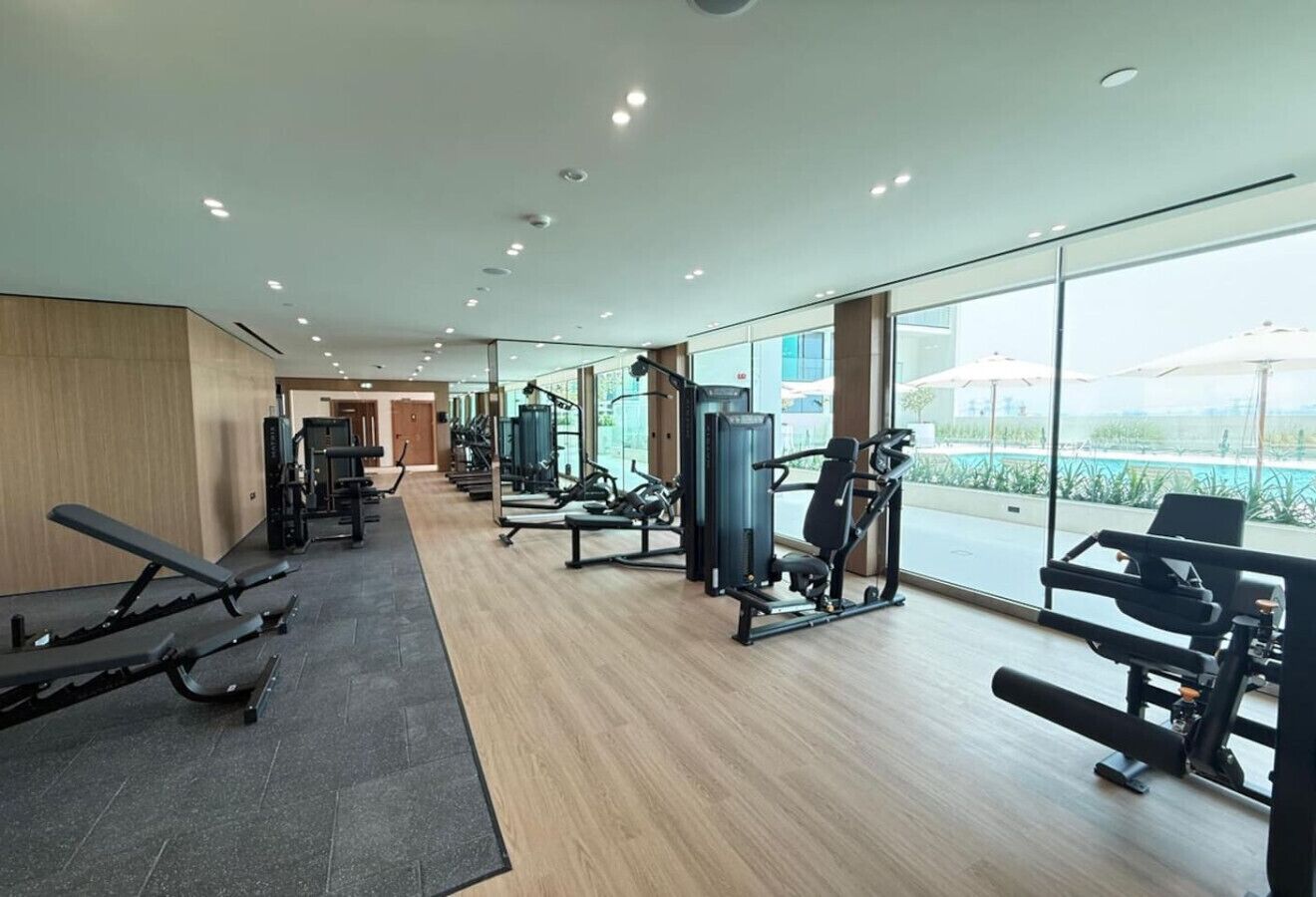 A modern gym with various exercise equipment, large windows, and a view of the outdoors.