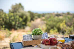 A table with a potted plant, a card, apples, a glass of juice, and a bowl of nuts.