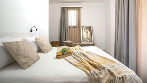 A neatly made bed with pillows and a blanket, a bedside table with a lamp, a framed picture on the wall, and a window with curtains.