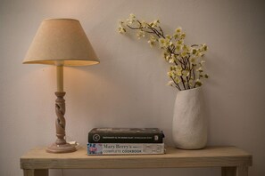 Uma luminária, um vaso com flores e uma pilha de livros sobre uma mesa de madeira.