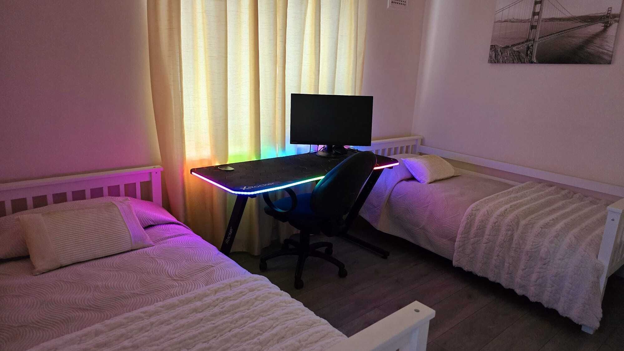 A bedroom with two single beds, a desk with a computer, and a window with curtains.