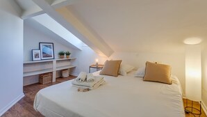 A bedroom with a large bed, a bedside table with a lamp, a small shelf with pictures and plants, and a wooden floor. - ATTIC URBAN AP4485 by Riviera Holiday Homes (Niza)