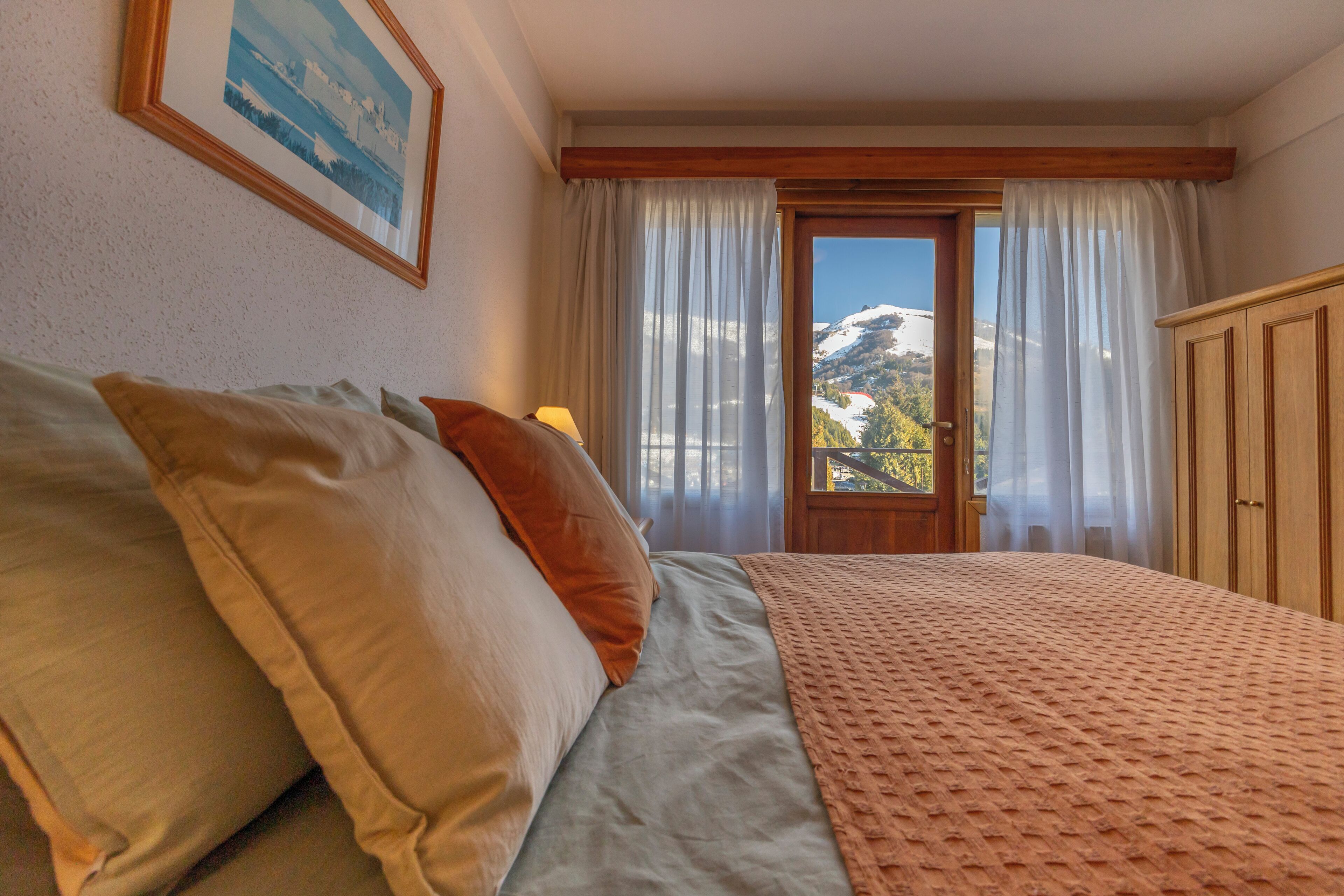 A bedroom with a bed, pillows, a window with curtains, and a view of a mountain.