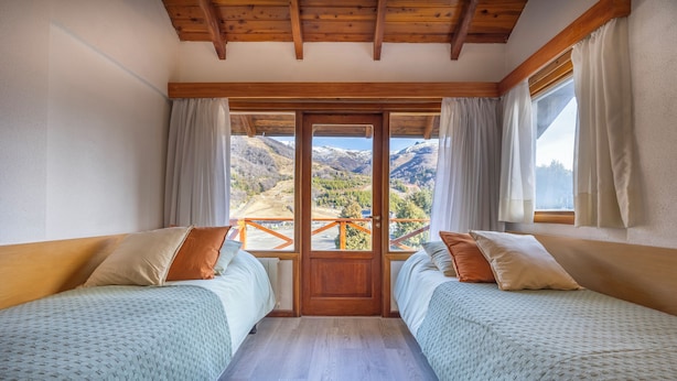 A room with two beds, wooden beams, a balcony with a railing, and a view of mountains. - Hotel Punta Condor (San Carlos de Bariloche)