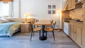 A compact room with a bed, a dining table with chairs, a kitchen area, and a small window with curtains. - Hotel Punta Condor (San Carlos de Bariloche)