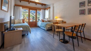 A bedroom with two beds, a desk, and a dining table with chairs. - Hotel Punta Condor (San Carlos de Bariloche)