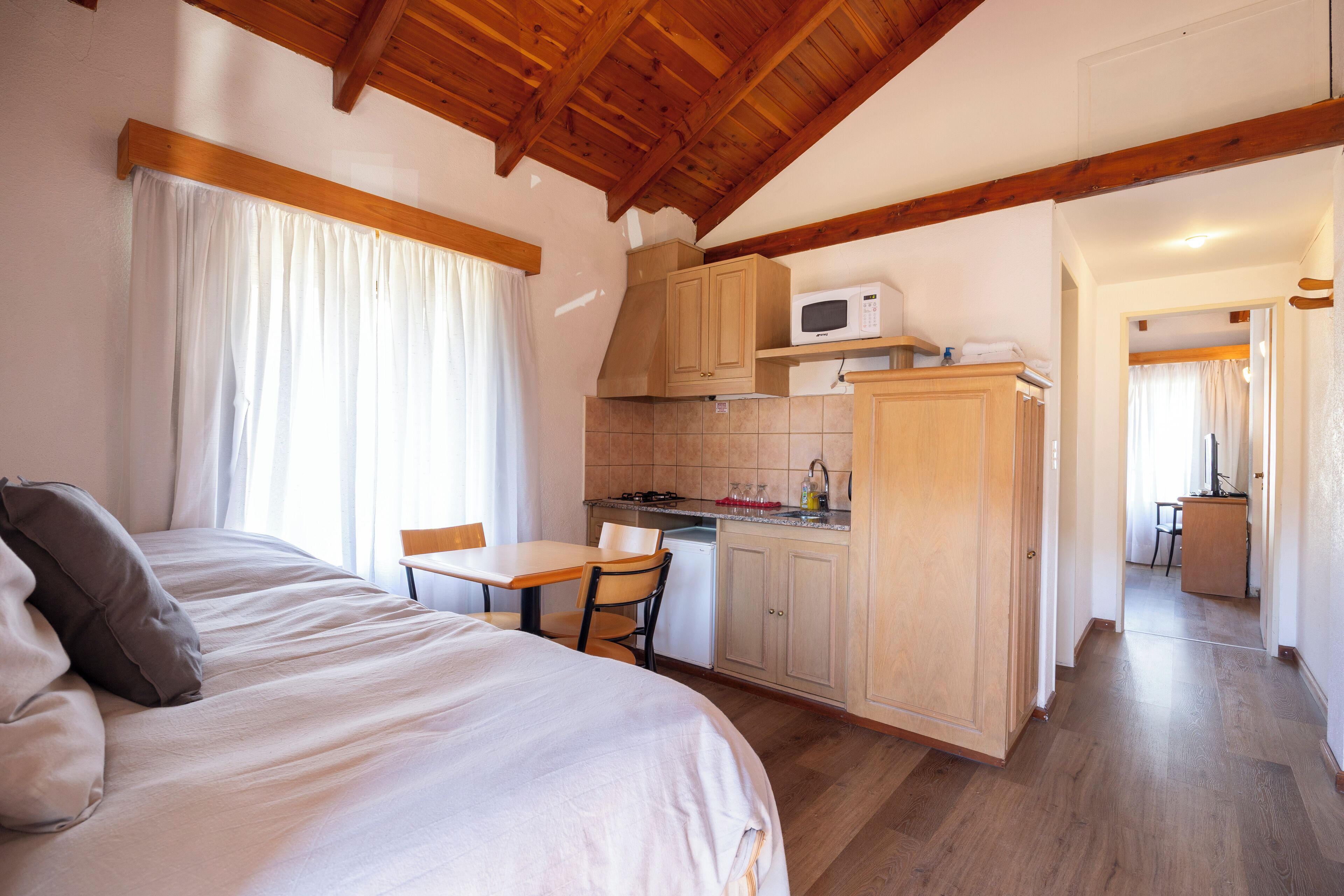 A bedroom with a bed, a desk, and a kitchenette.