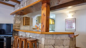 A bar area with a stone wall, wooden stools, and a television. - Hotel Punta Condor (San Carlos de Bariloche)
