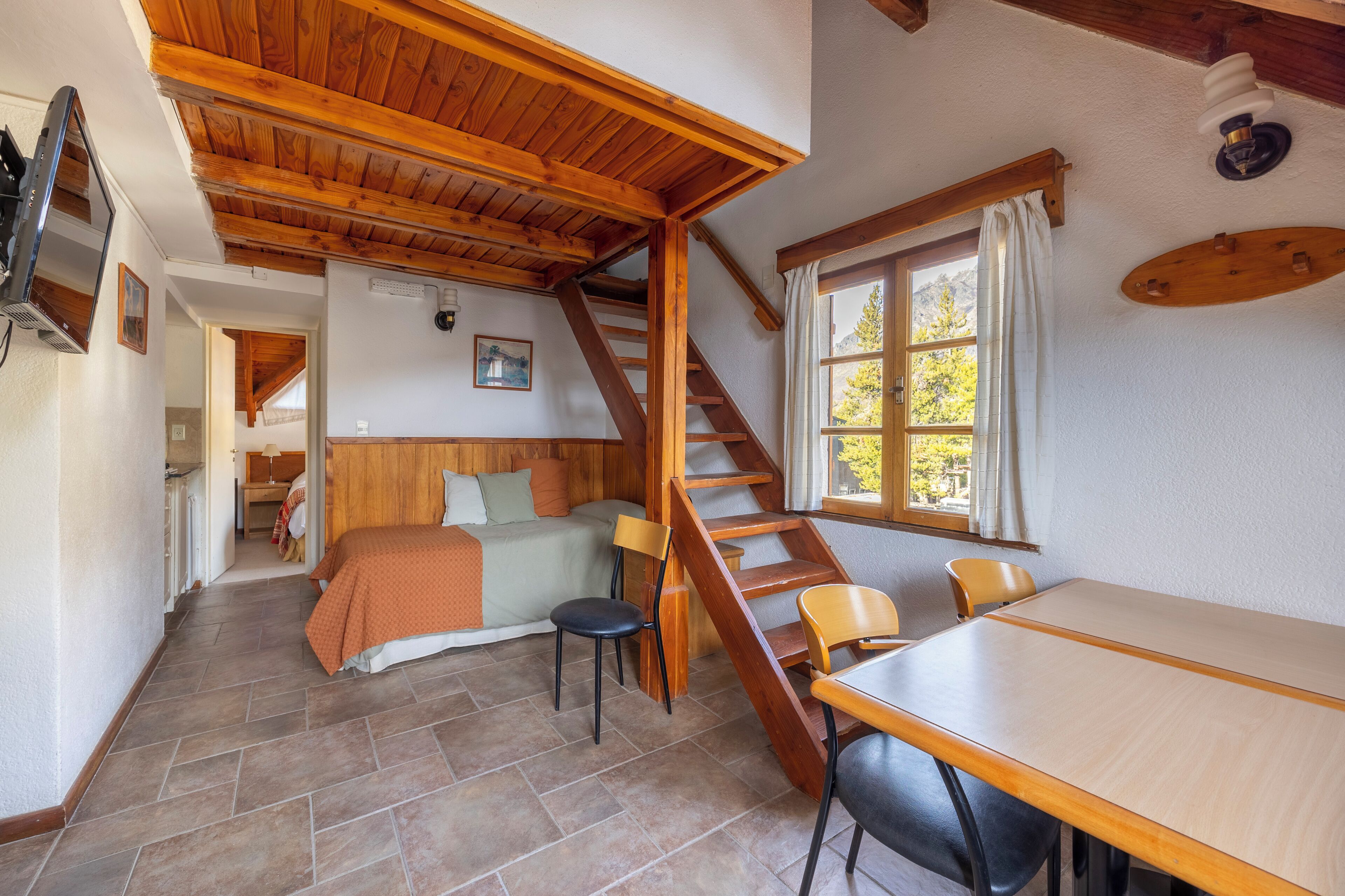 A cozy room with a bed, a dining table, and a staircase leading to another room.
