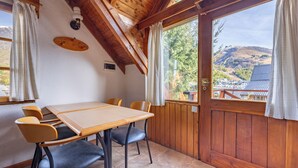 A wooden dining table with four chairs, a wooden ceiling, and a view of a mountain through a large window. - Hotel Punta Condor (San Carlos de Bariloche)
