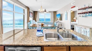A kitchen with granite countertops, stainless steel sinks, and a dining area with a view of the ocean. - ⭐Beach Front | GULF VIEWS | HUGE Balcony | Pool | Sterling Reef 501⭐ (Panama City Beach)