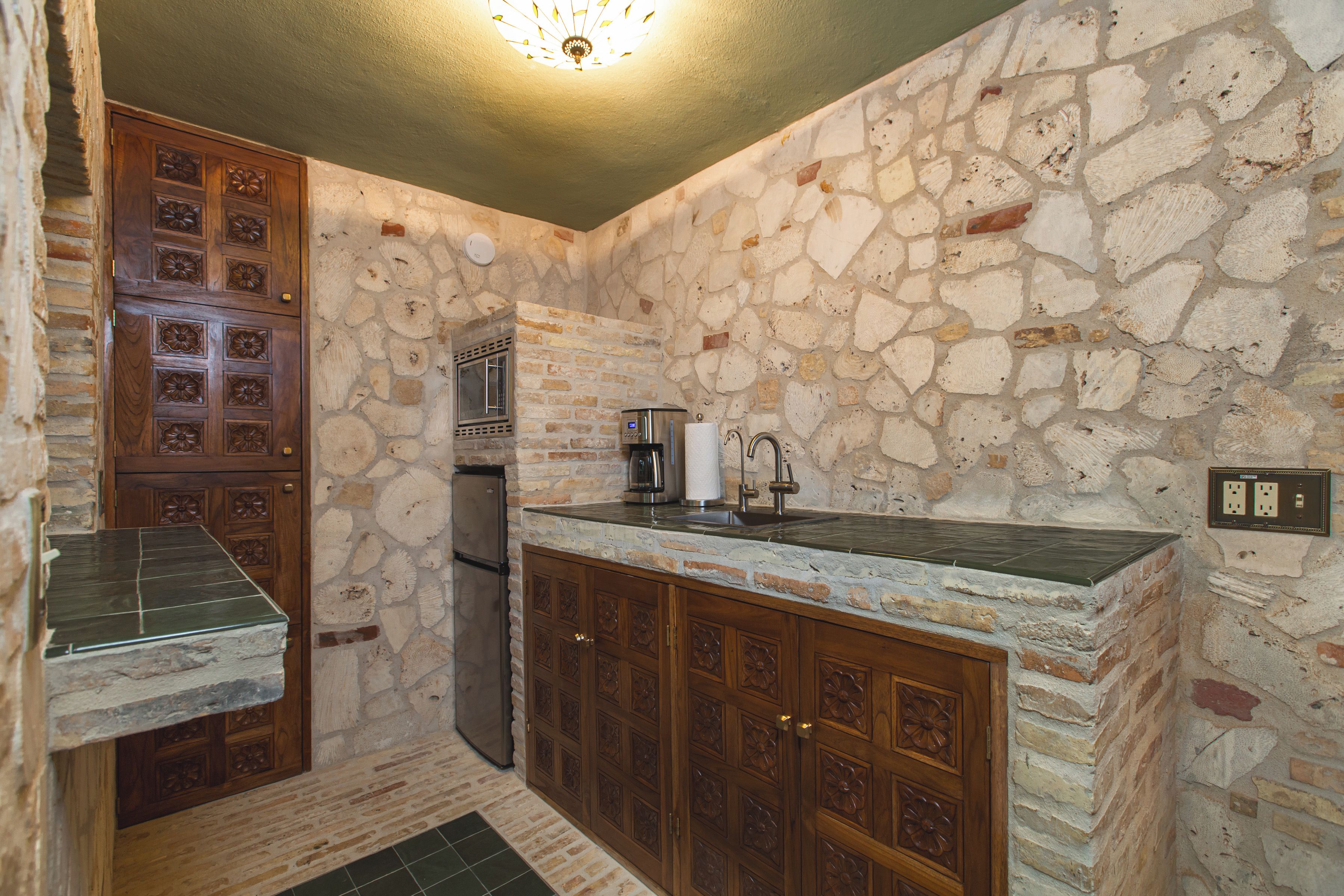 Cozinha com paredes de pedra, armários de madeira e geladeira embutida.
