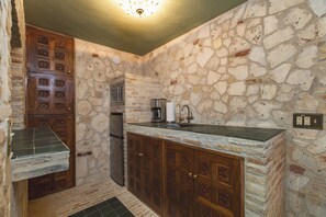 Una cocina con paredes de piedra, armarios de madera y un refrigerador empotrado.