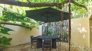 Een terras met een ronde tafel, stoelen, een parasol en een betegelde vloer.