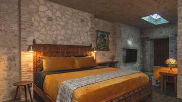 Un dormitorio con pared de piedra, cama de madera con cabecera, mesita de noche, lámpara y tragaluz.