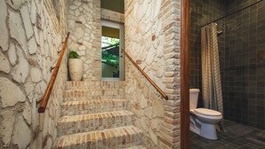Een badkamer met een toilet, een douche en een trap die naar een deur leidt.