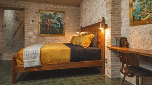 Een kamer met een bed, een bureau en een stoel. Er hangt een schilderij aan de muur en er is een trap.