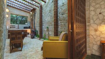 A cozy interior with a stone wall, a wooden door with intricate carvings, a yellow sofa, and a brick floor.
