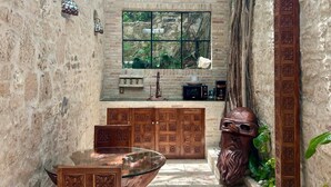 A stone-walled courtyard with a glass table, chairs, and a decorative wooden headpiece. - Treehouse - The Observatory (Christiansted)