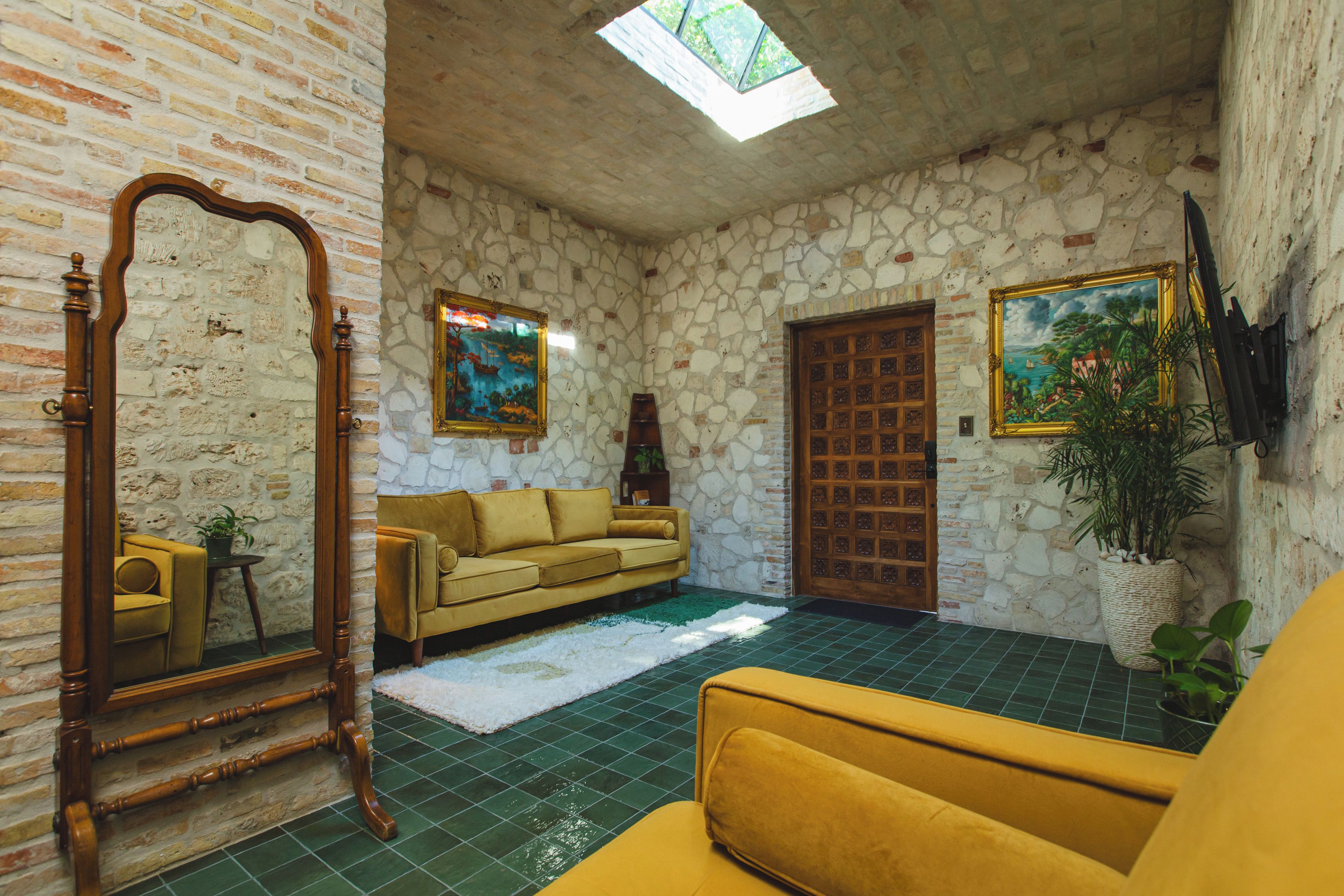 Ein Zimmer mit einer Steinwand, einer Holztür, einem gelben Sofa, einem großen Spiegel und einem Gemälde.