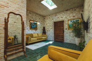 Una habitación con pared de piedra, puerta de madera, sofá amarillo, un espejo grande y un cuadro.