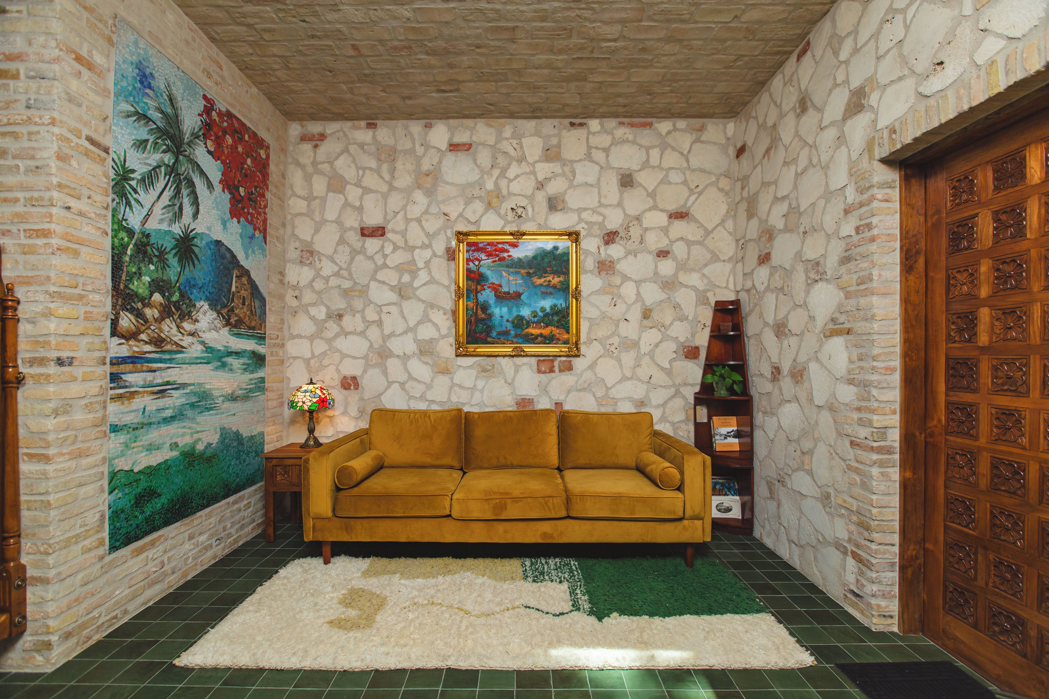 A room with a stone wall, a large painting, a sofa, a small table with a lamp, and a wooden door.