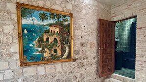 A room with a stone wall, a painting of a coastal scene, and a tiled floor. - Treehouse - The Observatory (Christiansted)