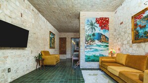 A room with a green tiled floor, a sofa, a chair, a television mounted on the wall, and a painting. - Treehouse - The Observatory (Christiansted)