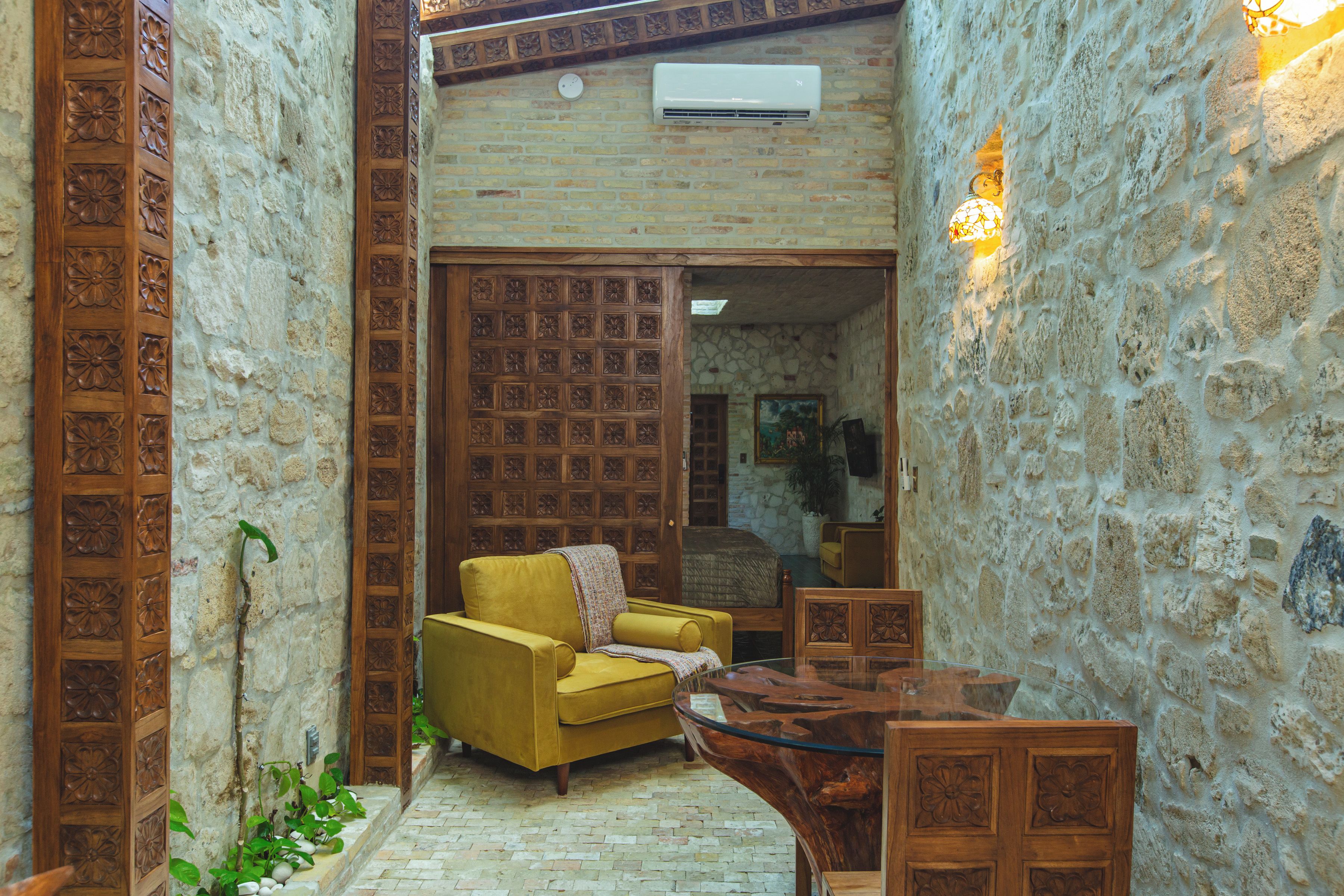 A narrow hallway with a yellow sofa, a wooden table, and a stone wall.