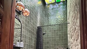 A bathroom with a sink, toilet, and shower area, featuring green tiled walls and a stained glass window. - Treehouse - The Observatory (Christiansted)