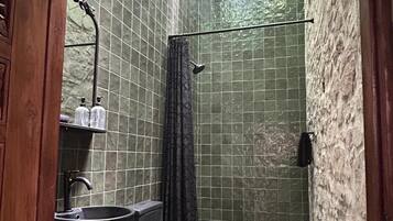 A bathroom with a sink, toilet, and shower area, featuring green tiled walls and a stained glass window.