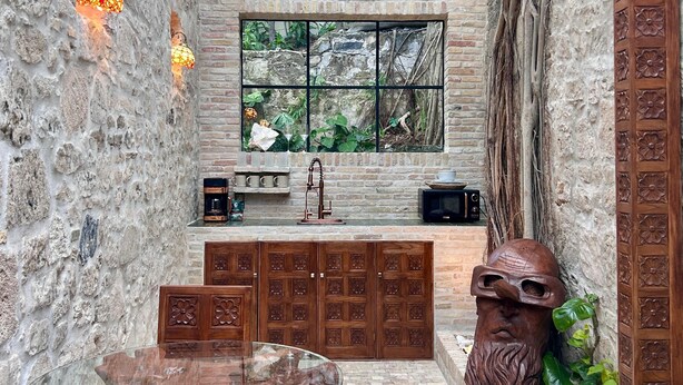 A narrow stone-walled kitchen with a window, a sink, and a wooden cabinet. - Treehouse - The Observatory (Christiansted)