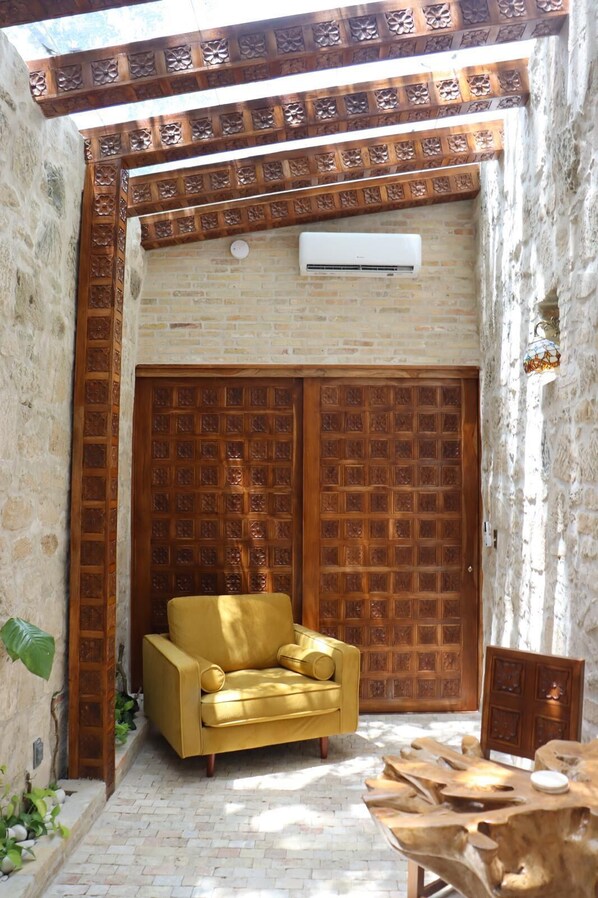 Una stanza accogliente con un divano giallo, una porta in legno finemente intagliata e un muro in pietra.