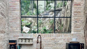 A kitchen with a rustic brick wall, a window with a jungle view, a coffee maker, a sink, and a microwave. - Treehouse - The Observatory (Christiansted)