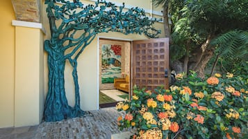 A doorway with a tree sculpture, a wooden door with floral carvings, and a garden with flowering plants.
