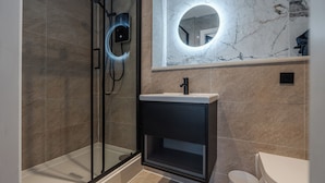 A modern bathroom with a glass shower enclosure, a pedestal sink, and a marble-tiled wall with a circular mirror. - Bold St ApartHotel | Book Individually or Book 8! (Liverpool)