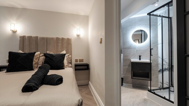 A modern hotel room with a large bed, a bedside table, a nightstand, and a glass-enclosed shower area. - Bold St ApartHotel | Book Individually or Book 8! (Liverpool)