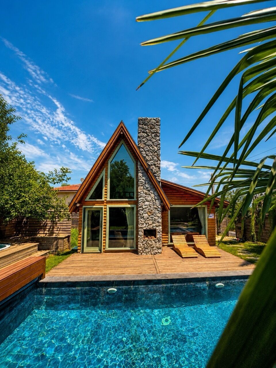 A modern house with a swimming pool, wooden deck, and stone chimney.
