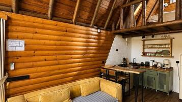 A log cabin interior with a wooden ceiling, a sofa, a small table, and a kitchen area.