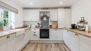 A modern kitchen with white cabinets, a stainless steel range hood, a built-in oven, and a wooden countertop. - BRAND NEW! Renovated luxury 2-bed cottage, parking & garden (Lechlade)