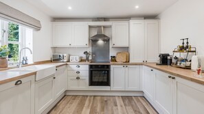 A modern kitchen with white cabinetry, a stainless steel range hood, a built-in oven, and a wooden countertop. - BRAND NEW! Renovated luxury 2-bed cottage, parking & garden (Lechlade)