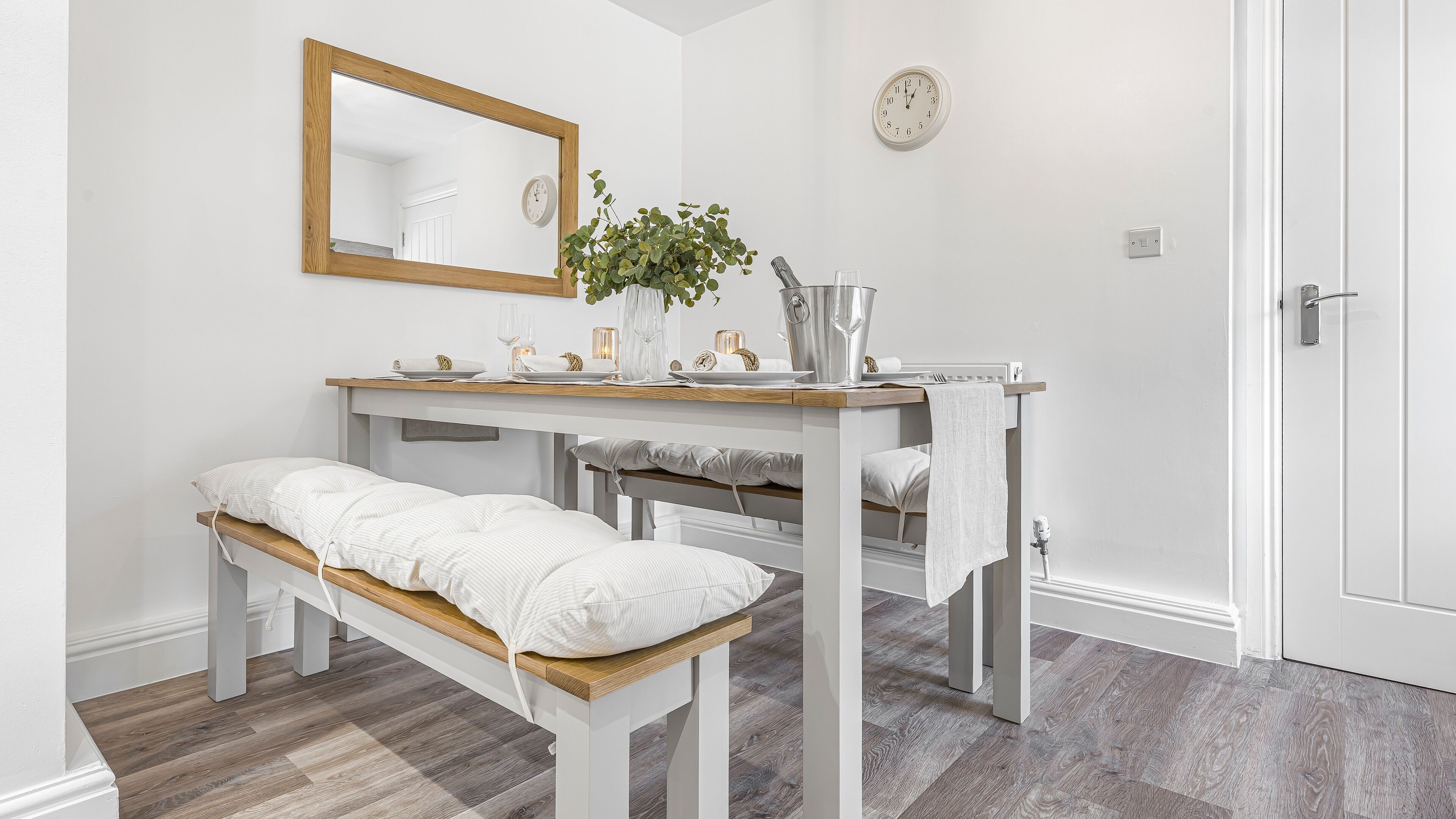 Ein Zimmer mit einer Holzbank, einem Tisch mit Spiegel, einer Uhr und einer Topfpflanze.