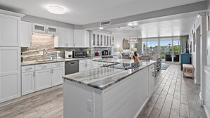 A spacious kitchen with white cabinetry, a large island, and a view to the outdoors.