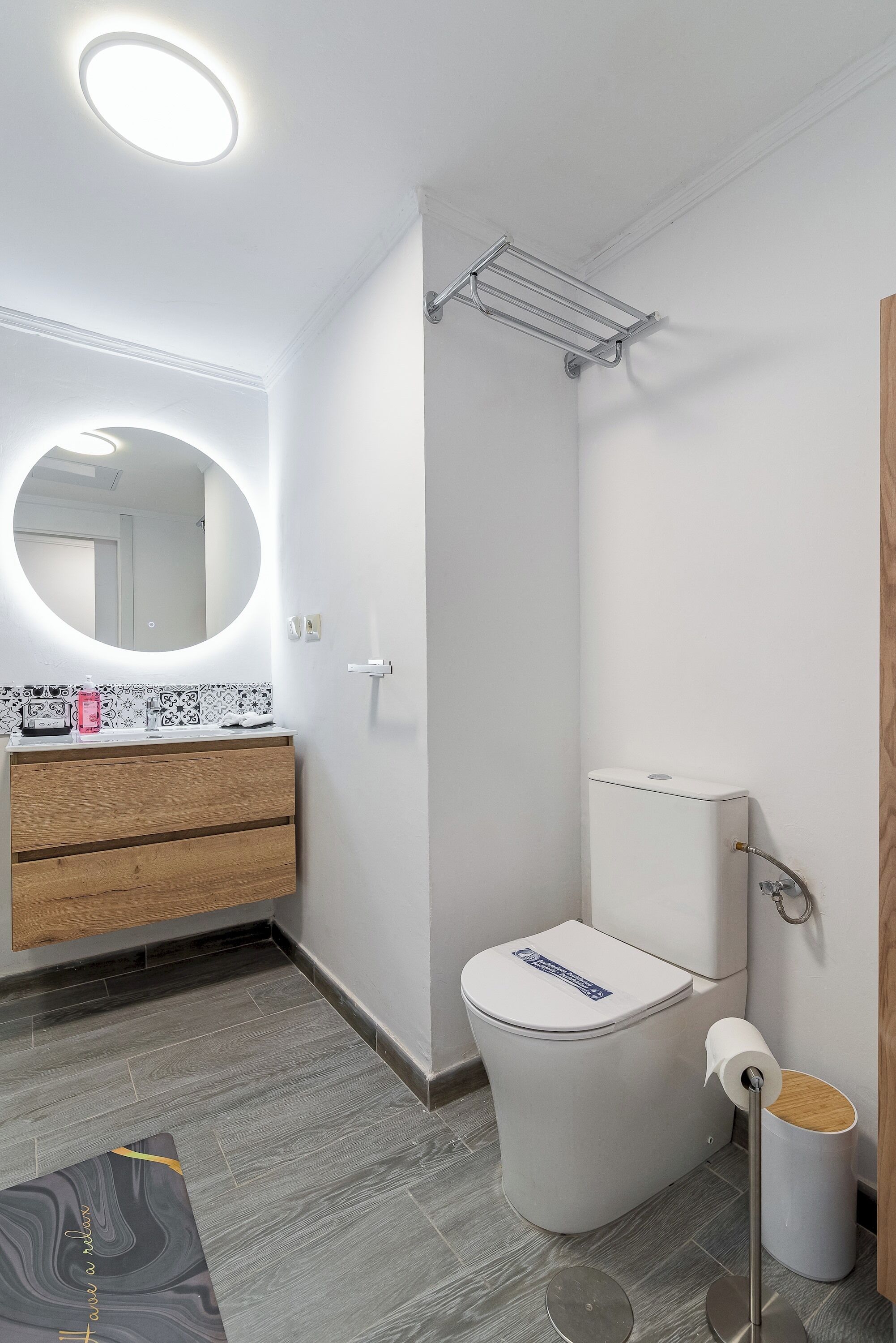 Un baño moderno con inodoro, lavamanos con espejo, ducha y dispensador de papel higiénico.