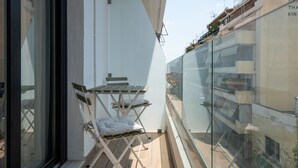 A balcony with a table and chairs, a glass railing, and a view of adjacent buildings.